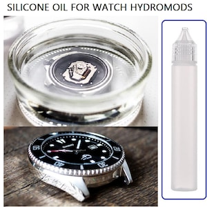 May include: Silicone oil for watch hydromods. The image shows a watch submerged in a glass container, a watch face, and a white plastic bottle with a clear tip. The watch face is black with white markings and a silver bezel.