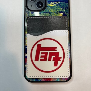 May include: A black phone case with a colorful abstract design and a white leather pocket with a red Toyota logo. The pocket has a stitched edge.
