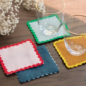 May include: Four colorful coasters with scalloped edges and a glass on each. The coasters are in shades of blue, green, yellow, and pink.