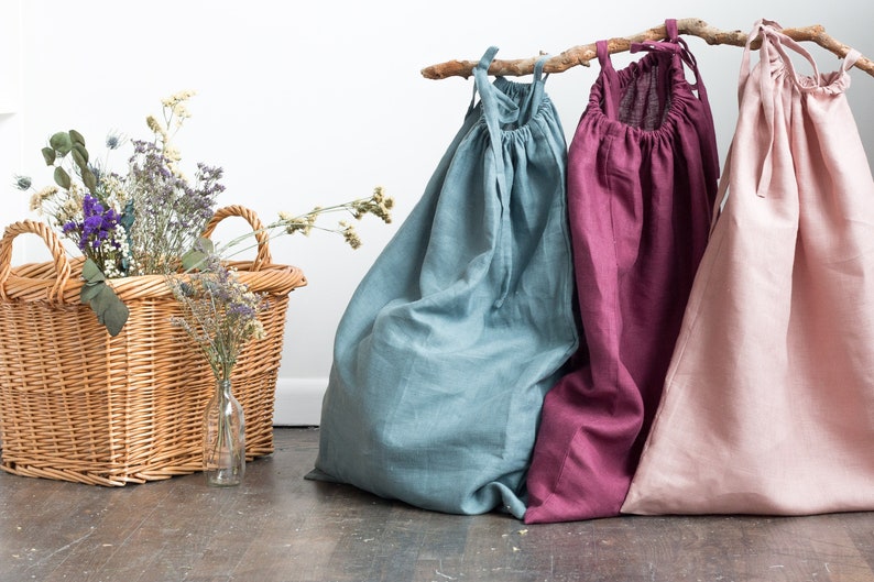 May include: Three linen drawstring bags in different colours: teal, burgundy, and blush pink. The bags are hanging from a branch and are arranged in a row.
