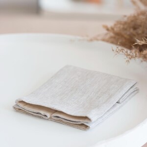 May include: A folded rectangular textile item featuring a light beige, textured outer layer with a visible woven grain and a smooth, solid light tan inner lining. The fabric is neatly layered, showing a clean edge and a neutral color palette.