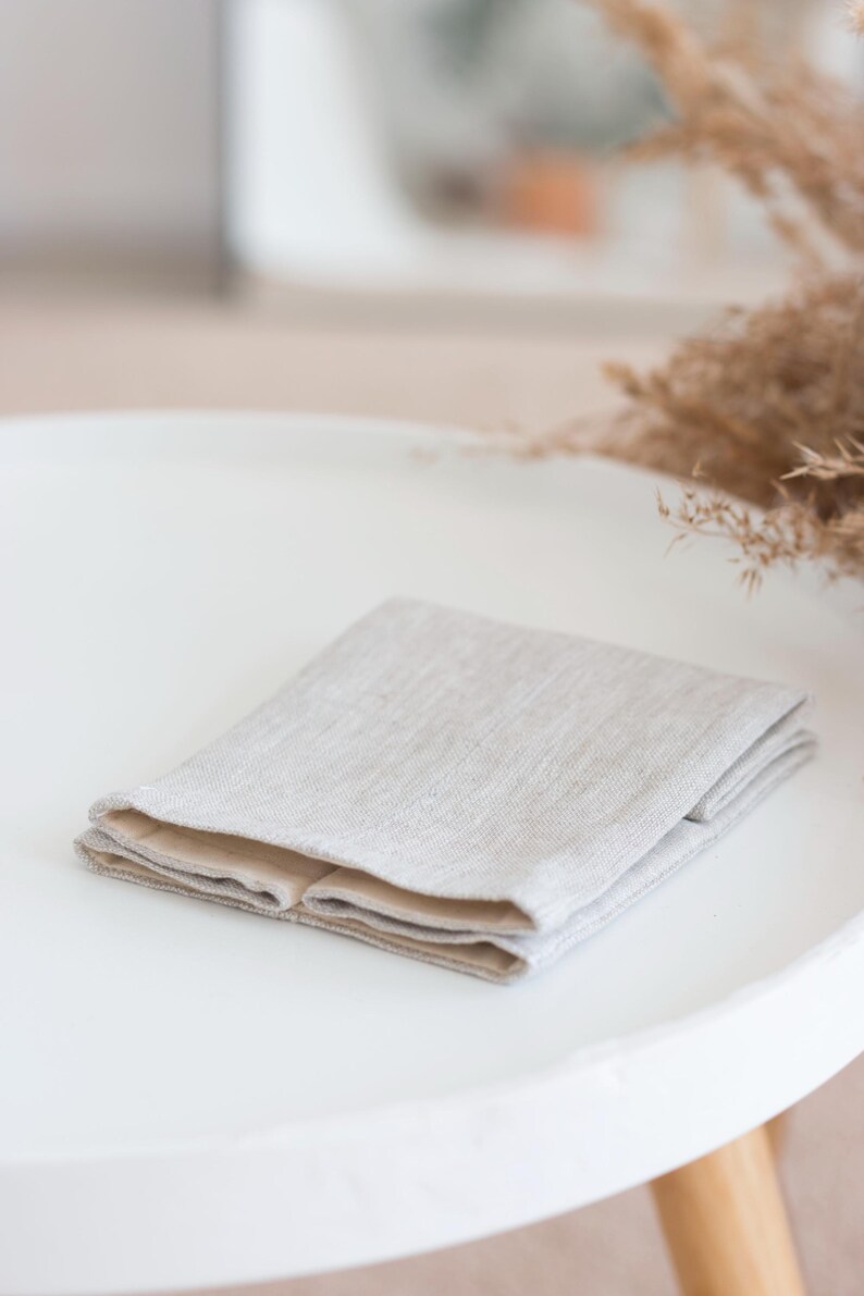 May include: A folded rectangular textile item featuring a light beige, textured outer layer with a visible woven grain and a smooth, solid light tan inner lining. The fabric is neatly layered, showing a clean edge and a neutral color palette.