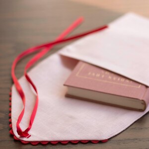 May include: A pink linen book cover with a red ribbon tie and a scalloped edge. A pink book with the title "Tanglewood Tales" is inside the cover.