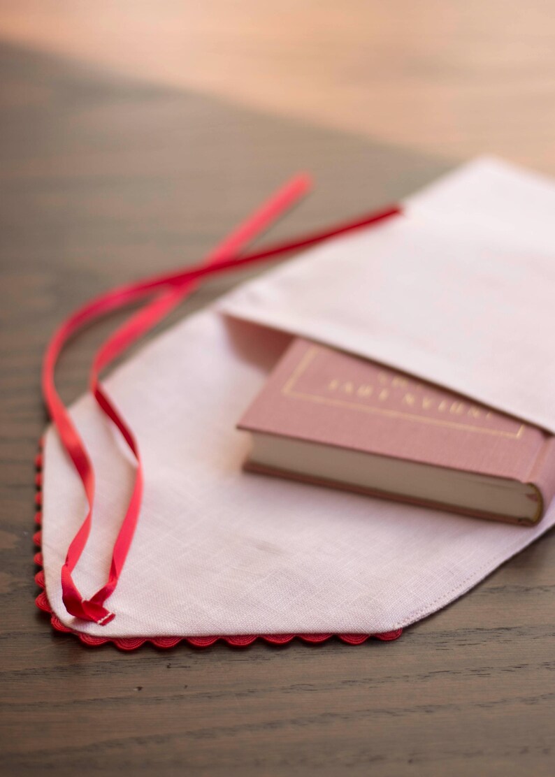 May include: A pink linen book cover with a red ribbon tie and a scalloped edge. A pink book with the title "Tanglewood Tales" is inside the cover.