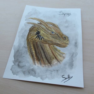 May include: Watercolor painting of a dragon's head, featuring shades of gold, brown, and blue. The dragon's head is detailed with textured scales and piercing blue eyes. The name "Syrax" is written at the top.