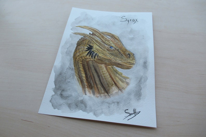 May include: Watercolor painting of a dragon's head, featuring shades of gold, brown, and blue. The dragon's head is detailed with textured scales and piercing blue eyes. The name "Syrax" is written at the top.