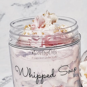 May include: A clear jar filled with pink whipped soap with gold sprinkles. The jar has a label that reads "Novelty Oils, A Soaps And Candles Studio, Whipped Soap, amber love, 4 oz."