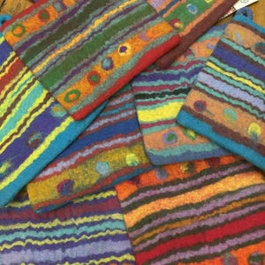 May include: A collection of colorful, hand-felted square pouches. Each pouch features horizontal stripes in various colors, including blue, green, orange, and purple, with decorative circular accents. The pouches have a textured appearance and a loop for hanging.