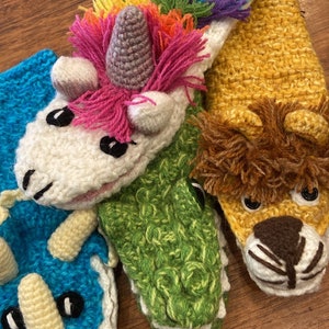 May include: Four crocheted finger puppets, each depicting a different animal. A white unicorn with a rainbow mane, a green alligator, a blue triceratops, and a yellow lion.