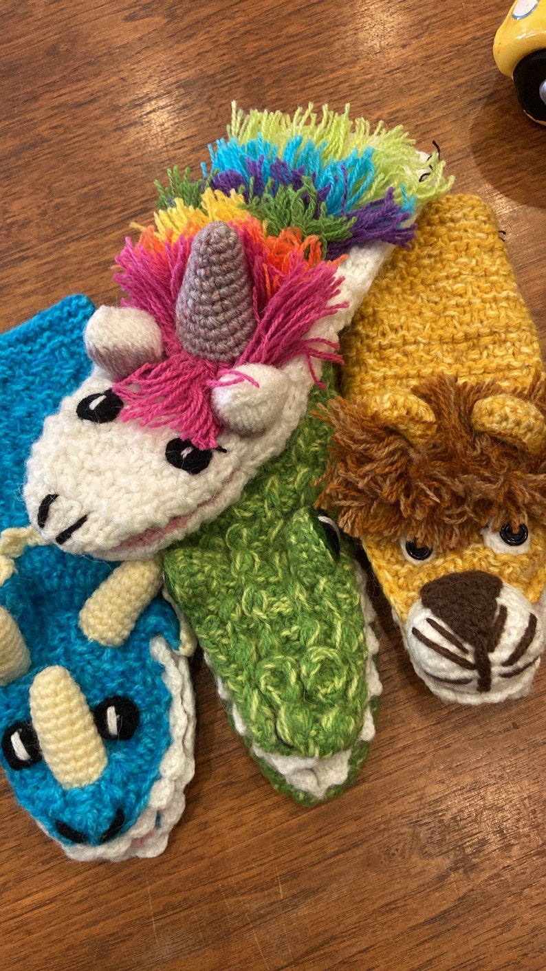 Pu&ograve; includere: Quattro marionette per dita all'uncinetto, ognuna raffigurante un animale diverso. Un unicorno bianco con una criniera arcobaleno, un alligatore verde, un triceratopo blu e un leone giallo.