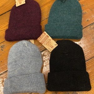 May include: Four knit beanies in different colors: burgundy, teal, gray, and black. Each beanie has a fold-over cuff and a small tag that says "Bandits Gifts".
