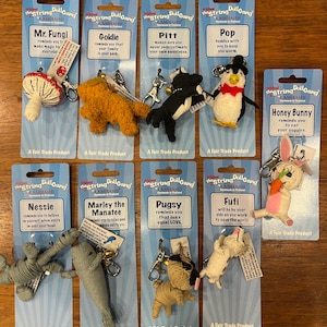 May include: Set of ten colorful string doll keychains with different animal designs. Each keychain has a tag with the name of the animal and a short message. The keychains are packaged on individual cards with a blue and white background.