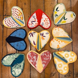 May include: Nine heart-shaped pot holders in various colors and patterns. The pot holders are made of fabric and have a quilted design. The patterns include floral, geometric, and abstract designs.