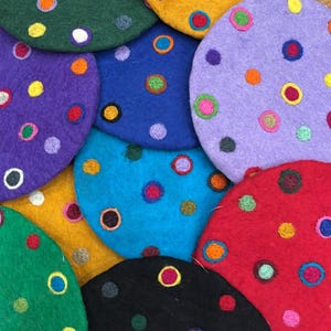 May include: A collection of colorful, round felt coasters. Each coaster is a different color, including green, yellow, purple, blue, and red. They are decorated with embroidered polka dots in various colors. These coasters are a fun and functional addition to any home.