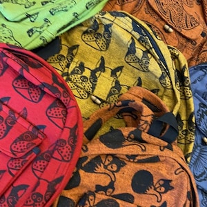 May include: Five different patterned backpacks. The backpacks are made of a soft, woven fabric and feature various animal prints. The prints include a green giraffe print, a yellow dog print, a red strawberry print, an orange cat print, and a blue floral print.