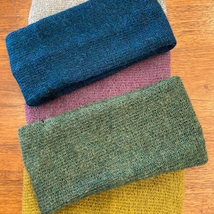 May include: Four knitted headbands in different colors: gray, teal, purple, green, and yellow. The headbands are stacked on top of each other.