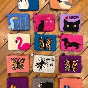 May include: A collection of 15 felt zipper pouches with various animal and nature designs. The pouches are in a variety of colors, including pink, blue, purple, orange, and gray. Some of the designs include an owl, a cat, a butterfly, a bee, a bear, and a bird.