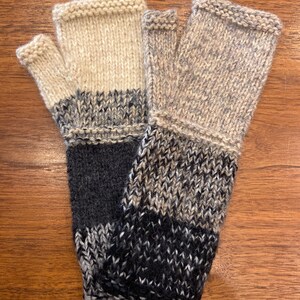 Op de afbeelding: Een paar vingerloze handschoenen met een zwart, grijs en beige breipatroon. De handschoenen zijn gemaakt van een zacht, warm materiaal en perfect om je handen in de winter warm te houden.