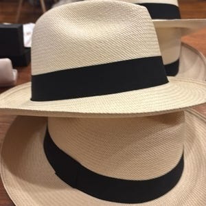 Puede incluir: Dos sombreros de paja con bandas negras. El sombrero de arriba tiene un ala ancha y el sombrero de abajo tiene un ala m&aacute;s estrecha.