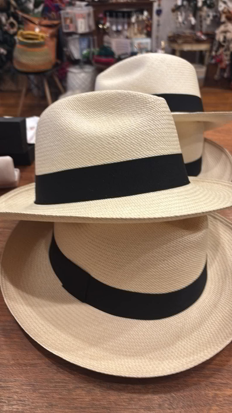 Puede incluir: Dos sombreros de paja con bandas negras. El sombrero de arriba tiene un ala ancha y el sombrero de abajo tiene un ala m&aacute;s estrecha.