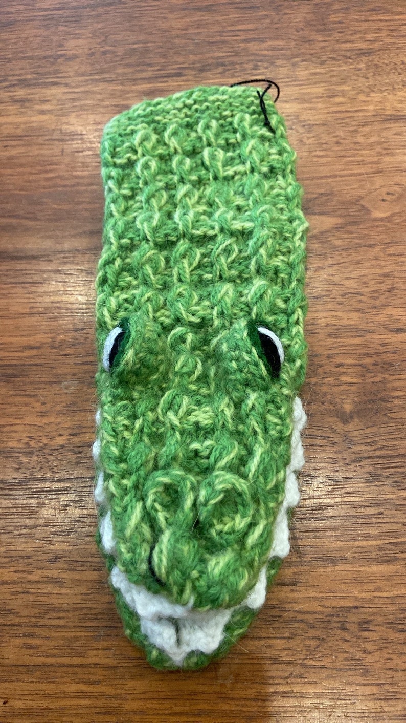 Pu&ograve; includere: Marionetta di coccodrilo in crochet verde con denti bianchi e occhi neri.