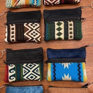 May include: Eight colorful zippered pouches with keychains. Each pouch has a black fabric top and a patterned bottom. The patterns are geometric and feature a variety of colors, including red, blue, green, yellow, and brown.
