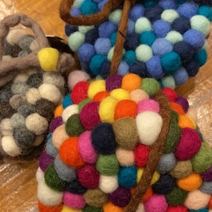 May include: Three round felt coasters with a brown felt cord wrapped around them. The coasters are made of small felt balls in various colors, including blue, green, yellow, red, orange, and purple.