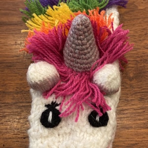 Pu&ograve; includere: Un unicorno bianco all'uncinetto con una criniera arcobaleno e un corno grigio. L'unicorno ha occhi neri e un naso rosa.