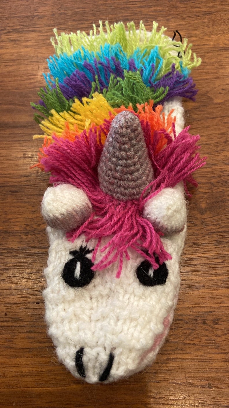 Pu&ograve; includere: Un unicorno bianco all'uncinetto con una criniera arcobaleno e un corno grigio. L'unicorno ha occhi neri e un naso rosa.