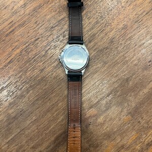 May include: A silver-toned wristwatch with a black leather band. The watch face is not visible, but the back of the watch is visible, with text and a logo. The band is marked "Genuine Leather".