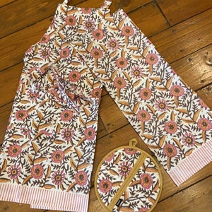 May include: A white apron with a floral print in shades of pink, orange, and brown. The apron has a pink and white striped border. A matching floral pot holder is included.