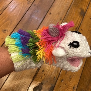 Pu&ograve; includere: Un pupazzo di mano di unicorno bianco all'uncinetto con una criniera arcobaleno e un corno rosa. Il pupazzo ha occhi neri e una bocca rosa.