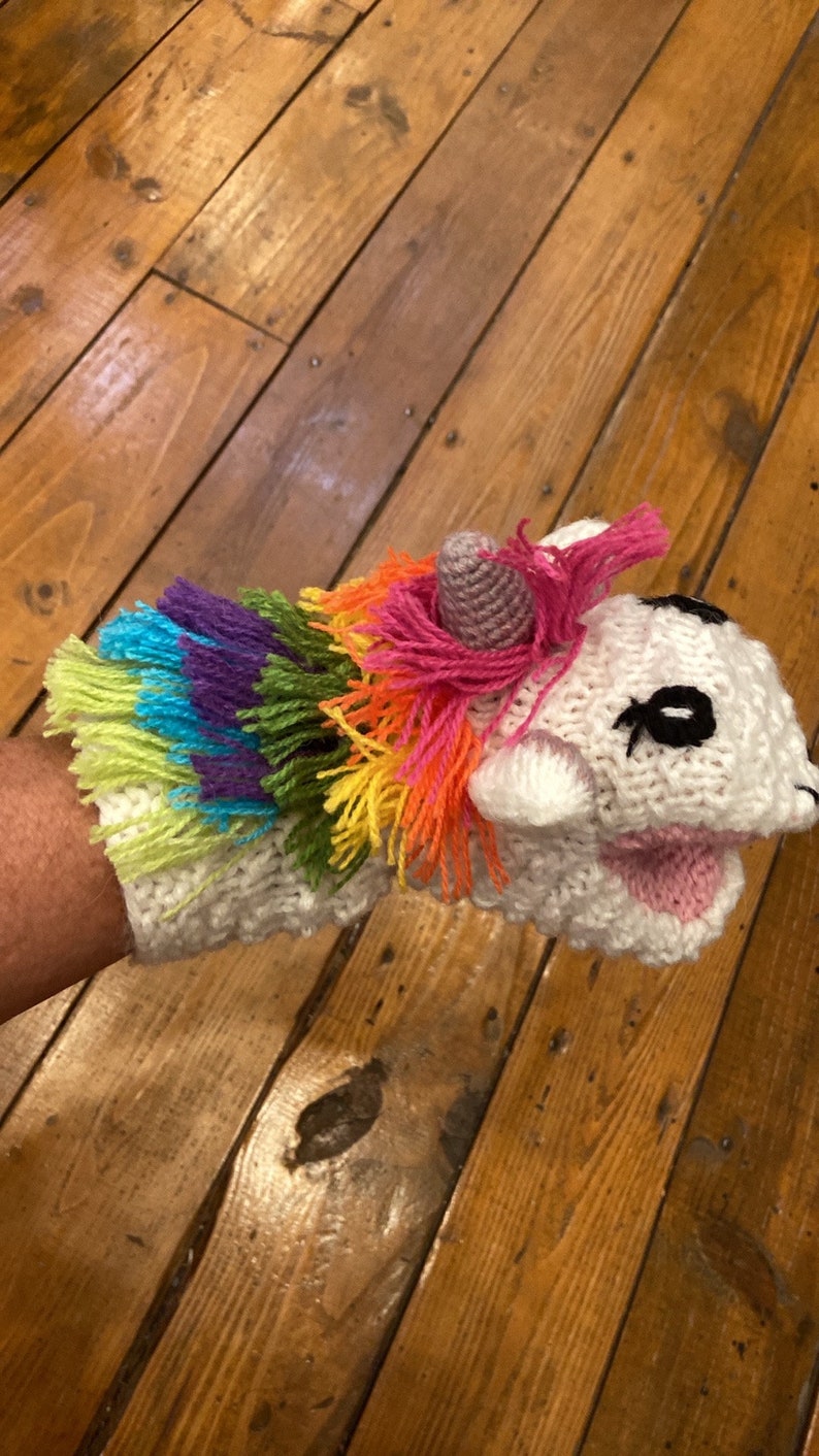 Pu&ograve; includere: Un pupazzo di mano di unicorno bianco all'uncinetto con una criniera arcobaleno e un corno rosa. Il pupazzo ha occhi neri e una bocca rosa.