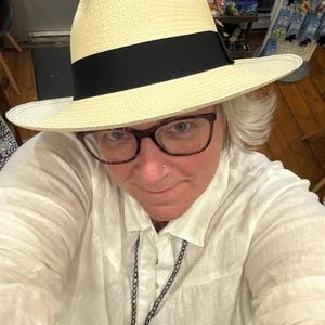 Puede incluir: Una persona que lleva una camisa blanca y un sombrero de paja con una banda negra. El sombrero tiene un ala ancha y est&aacute; hecho de un material tejido.