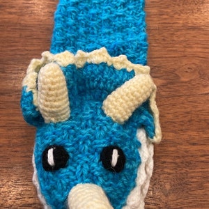 Pu&ograve; includere: Un pupazzo a mano in crochet blu a forma di triceratopo con corna e occhi bianchi.