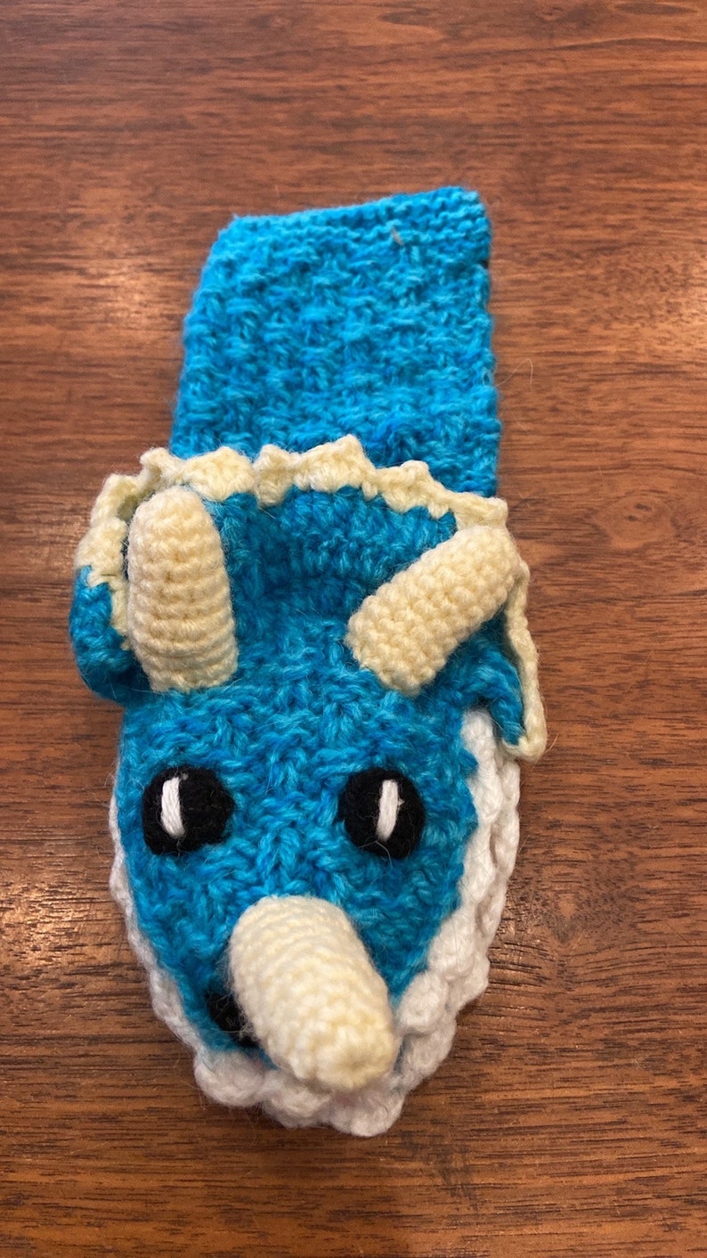 Pu&ograve; includere: Un pupazzo a mano in crochet blu a forma di triceratopo con corna e occhi bianchi.