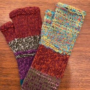 Op de afbeelding: Een paar kleurrijke vingerloze handschoenen met een gestreept patroon. De handschoenen zijn gemaakt van een zachte, gebreide stof en hebben een verscheidenheid aan kleuren, waaronder rood, oranje, geel, groen, blauw en paars.