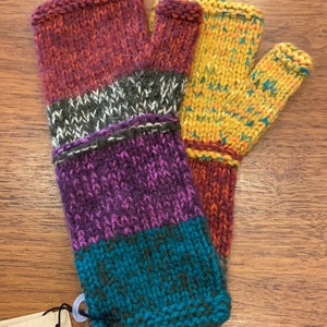 Op de afbeelding: Een paar kleurrijke vingerloze handschoenen met een gestreept patroon in tinten rood, paars, turquoise en geel. De handschoenen zijn gemaakt van gebreide wol en hebben een label met de tekst "Met liefde gebreid in de hooglanden van Bolivia".