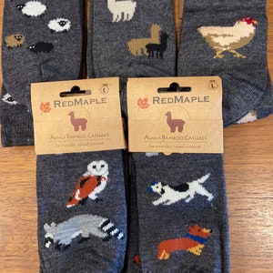 May include: Four pairs of gray alpaca bamboo casual socks with different animal designs. The socks feature a llama, a chicken, an owl, and a dog. The socks are packaged in brown cardboard with the brand name "RedMaple" printed on them.
