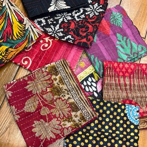 May include: A collection of colorful, square fabric coasters with various patterns. Designs include floral, geometric, and polka dots in shades of red, yellow, black, and purple. Each coaster is stitched with contrasting thread.