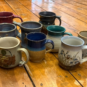 May include: A collection of ten ceramic mugs with various colors and patterns. The mugs are all handmade and have a rustic look. Some of the mugs have floral designs, while others have geometric patterns.