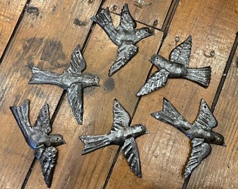 May include: A collection of five silver-toned metal bird ornaments, each featuring detailed wing and tail feather textures. Every bird is depicted in a flying pose with wings extended, and each includes a small hole at the top for hanging purposes.