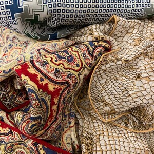 May include: A collection of three patterned fabric squares. The top square is a geometric pattern in shades of blue, green, and white. The middle square is a paisley pattern in shades of red, yellow, blue, and white. The bottom square is a brown and white snake skin pattern.