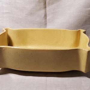 Può includere: Un piatto rettangolare in ceramica giallo chiaro con finitura maculata. Il piatto ha un bordo ondulato e decorativo, probabilmente per servire o esporre. Il colore neutro e il design semplice lo rendono versatile.