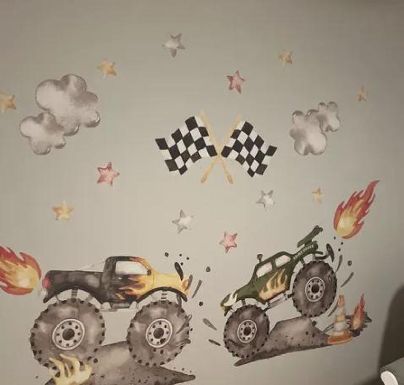 May include: Wall stickers depicting two monster trucks with flames and dirt effects. The design includes checkered flags, clouds, and star accents, creating a dynamic scene. The trucks are in shades of black, yellow, and green, suitable for a child's room.