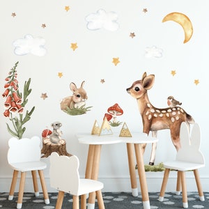 May include: A white table and chairs with a woodland theme. The wall has decals of a deer, rabbit, clouds, stars, mushrooms, and a bird. The chairs have bunny ears.