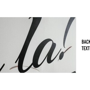 May include: Close-up of a white backdrop with black cursive text that reads "la!". The backdrop has a textured surface. The words are in a bold, elegant font.