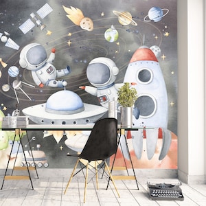 May include: A watercolor illustration of a space scene with two astronauts, a rocket ship, planets, and stars. The background is a dark blue with white stars. The astronauts are wearing white spacesuits with blue helmets. The rocket ship is red and white with a blue flame. The planets are various colors and sizes. The stars are white and yellow.