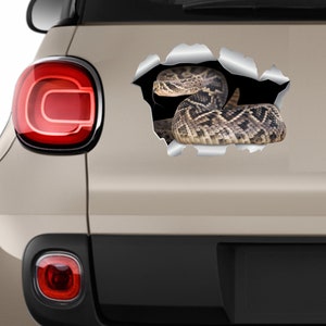 May include: A realistic vinyl sticker of a rattlesnake peeking out of a ripped hole in a car. The snake is brown and tan with black markings. The sticker is perfect for adding a touch of danger to any vehicle.