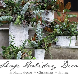 May include: Arrangement of greenery and berries in white birch bark containers. The containers are arranged on a stone surface. The image includes the text "Shop Holiday Decor" and "Holiday decor + Christmas + Home".